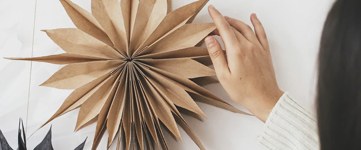 O mână atinge o stea de origami din hârtie maro