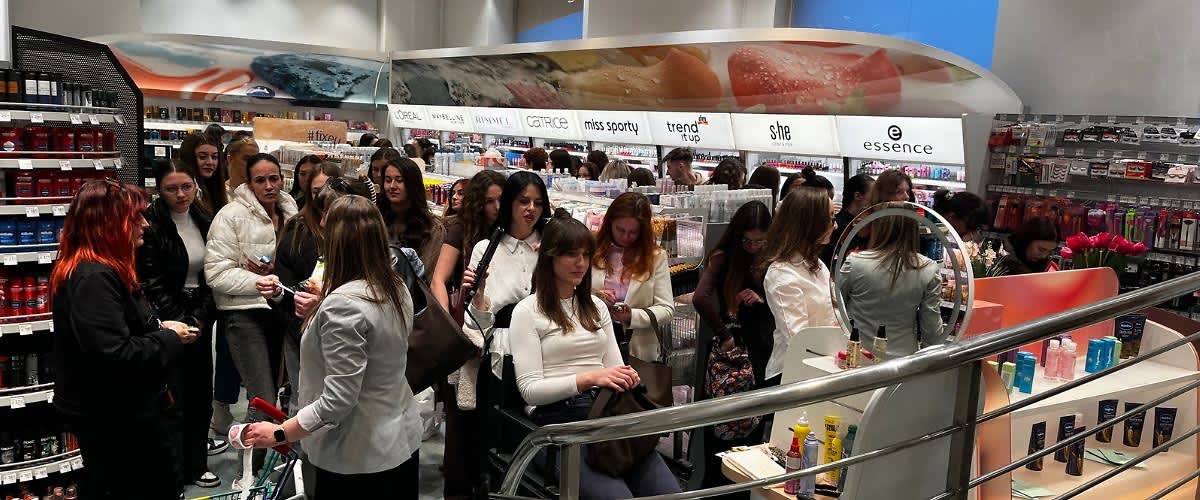 Magazin cosmetic aglomerat cu multe cliente care răsfoiesc produse și vânzătoare
