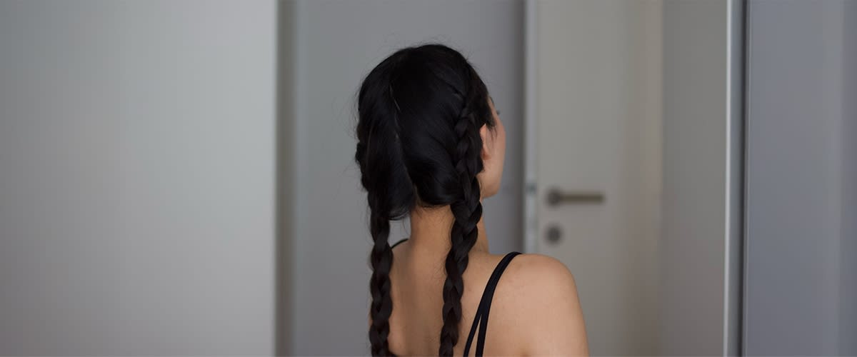 Persoană văzută din spate cu părul în două cozi împletite și bretele negre vizibile