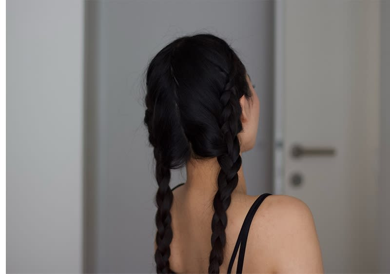 Persoană văzută din spate cu părul în două cozi împletite și bretele negre vizibile
