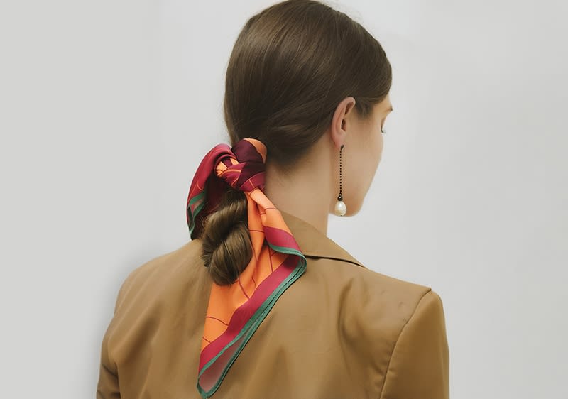 Femeie văzută din spate cu păr prins în coc și eșarfă colorată cu model geometric

