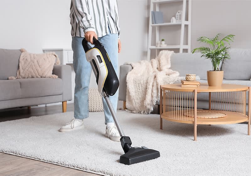 Persoană aspirând covorul din sufragerie cu aspirator vertical fără fir