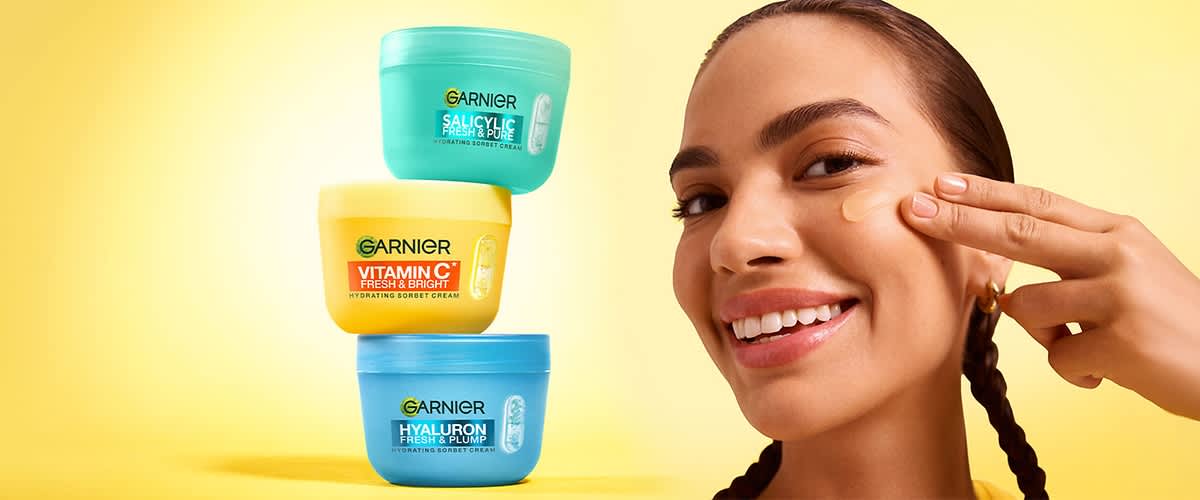 Produse cosmetice Garnier stivuite lângă fața unei femei care își împletește părul