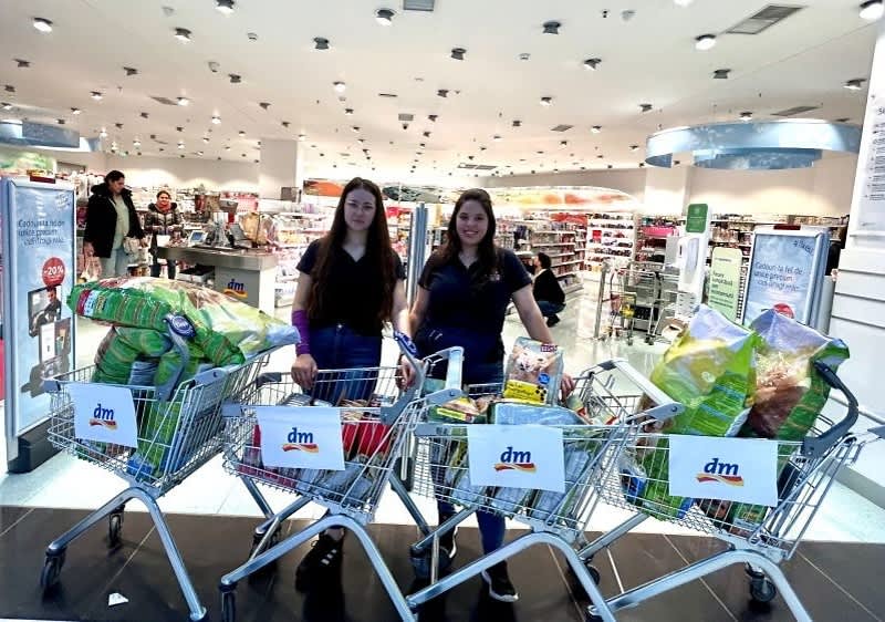 Două femei zâmbitoare cu trei cărucioare pline de cumpărături într-un magazin dm