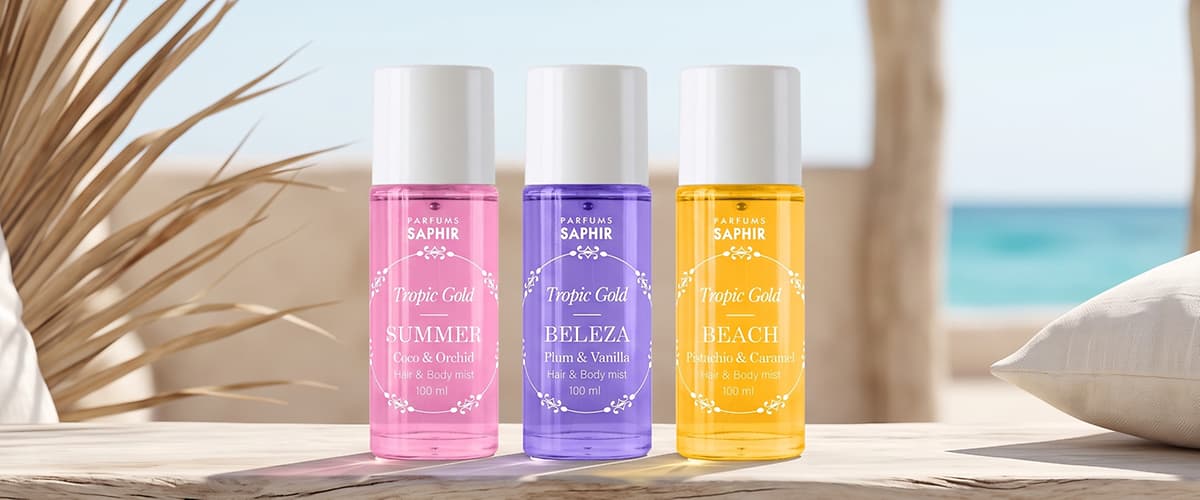 Parfum Tropic Gold cu trei spray-uri roz mov galben așezate pe lemn cu fructe și flori