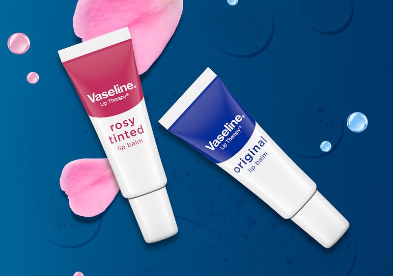 Două tuburi de balsam de buze Vaseline rosé tinted și original pe fundal albastru cu petale de trandafir