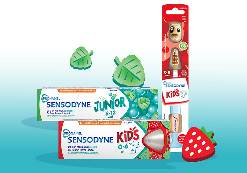 Periuță de dinți pentru copii Sensodyne în ambalaj alături de paste de dinți Junior și Kids și decorațiuni căpșuni și frunze