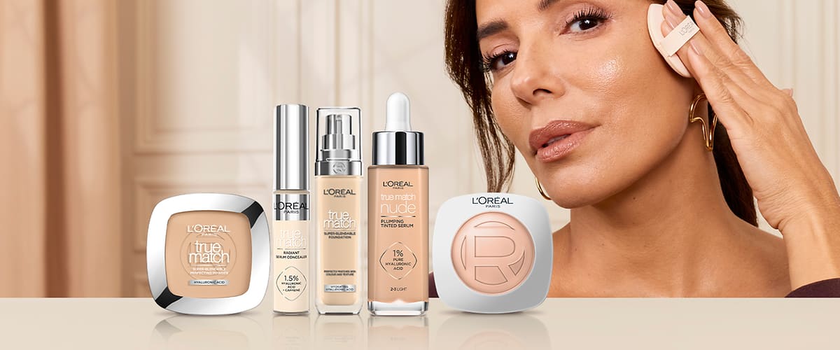 Pe fundal bej deschis, cinci produse L'Oréal True Match aranjate în linie: de la stânga la dreapta pudră compactă pătrată bej în ambalaj alb cu margine metalică și inscripția „L'Oréal True Match”, un recipient subțire cu pompă argintie etichetat „True Match 1.5%”, un flacon cu pompă transparentă și lichid bej scris „True Match Foundation”, un ser cu pipetă etichetat „True Match Nude 1% Acid Hialuronic” într-un flacon cu capac argintiu și o pudră compactă rotundă albă cu logo-ul L'Oréal și nuanță bej