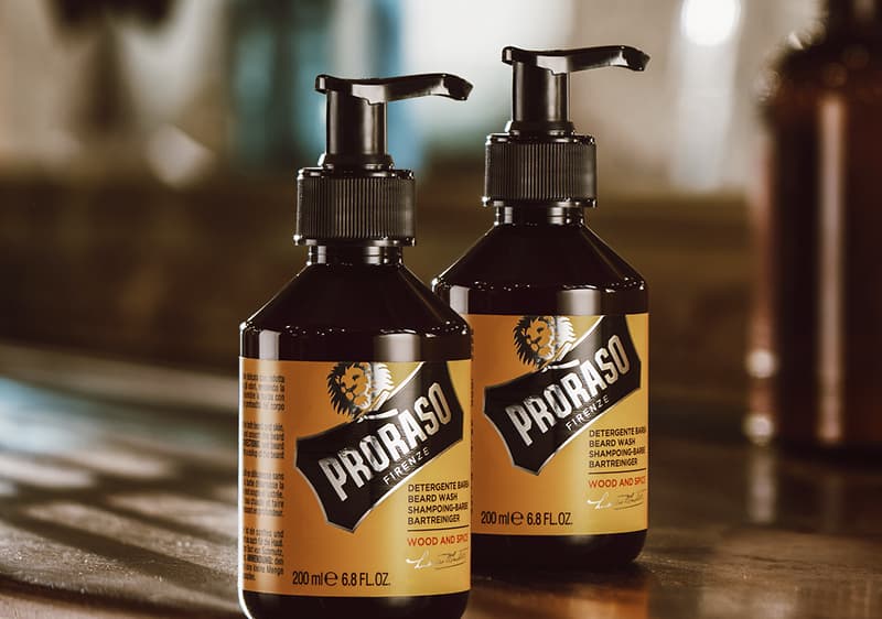 Două sticle pompiță maro-închis de 200 ml de șampon/gel de bărbierit Proraso cu etichetă galbenă și logo alb-negru, text „Proraso” și mențiune „Wood and Pine” așezate pe o suprafață lucioasă, una în față și una parțial vizibilă în spate