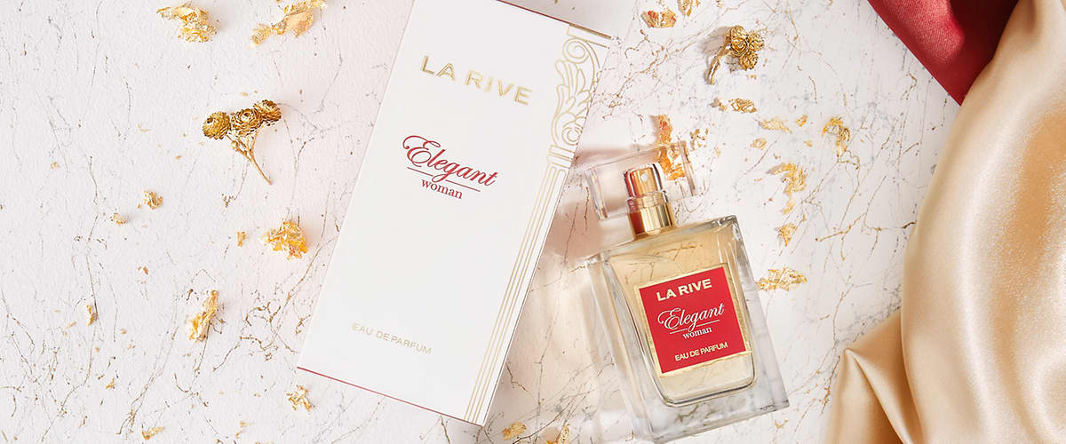 Cutie albă și aurie cu inscripția „LA RIVE Elegant woman Eau de Parfum” alături de sticlă pătrată de parfum transparentă cu lichid galben pal și etichetă roșie „LA RIVE Elegant woman” pe un fundal marmorat cu foilețe aurii și satin bej