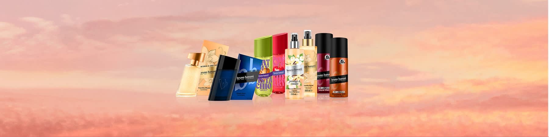 Pe fundal roz-piersică cu nuanțe de apus, cinci produse Bruno Banani plasate în stânga: două spray-uri pentru corp galbene cu flori și text „bruno banani” și „250 ml”, un recipient roz deschis, un deodorant spray negru-portocaliu etichetat „bruno banani” și un flacon negru-portocaliu mai mic