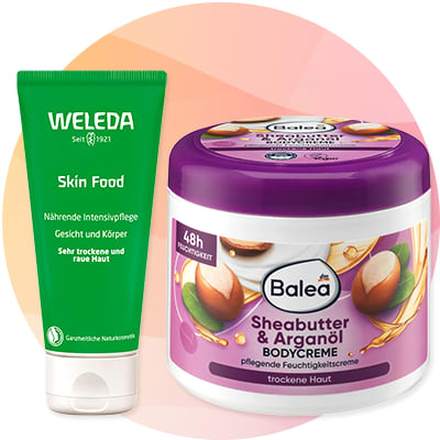 Zelené tubové balenie Weleda Skin Food s bielym uzáverom a nemeckým textom, vedľa biele plastové dózy Balea Sheabutter & Arganöl bodycreme s fialovým viečkom a obrázkami orechov a arganového plodu na etikete