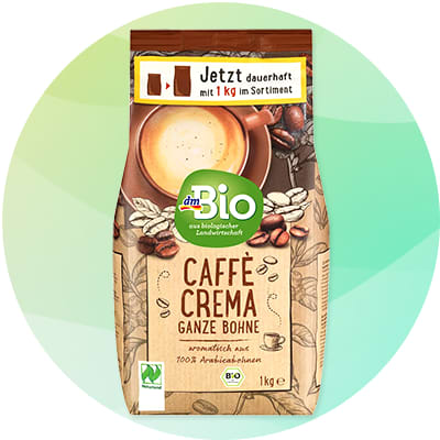 Balenie dmBio Caffè Crema celé zrno 1 kg so zeleným kruhovým logom „dmBio“, obrázkom šálky kávy v hornej časti, nápisom „Caffè Crema Ganze Bohne“ a symbolmi bio certifikátu a hmotnosti 1 kg