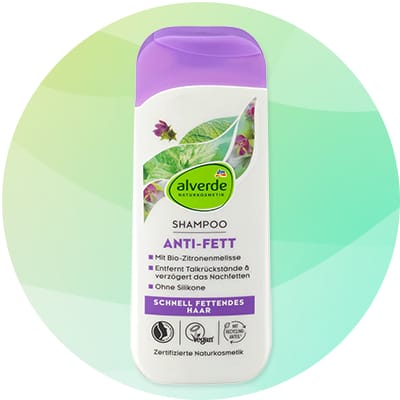 Biela fľaša šampónu Alverde s fialovým uzáverom, na prednej strane zelené listy a nápis „ANTI-FETT“, text „SHAMPOO“ a značka „alverde NATURKOSMETIK“, označenia vegánske a certifikované prírodné kozmetika