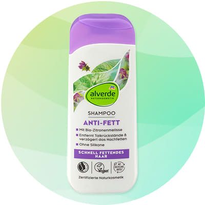Biela fľaša šampónu Alverde s fialovým uzáverom, na prednej strane zelené listy a nápis „ANTI-FETT“, text „SHAMPOO“ a značka „alverde NATURKOSMETIK“, označenia vegánske a certifikované prírodné kozmetika