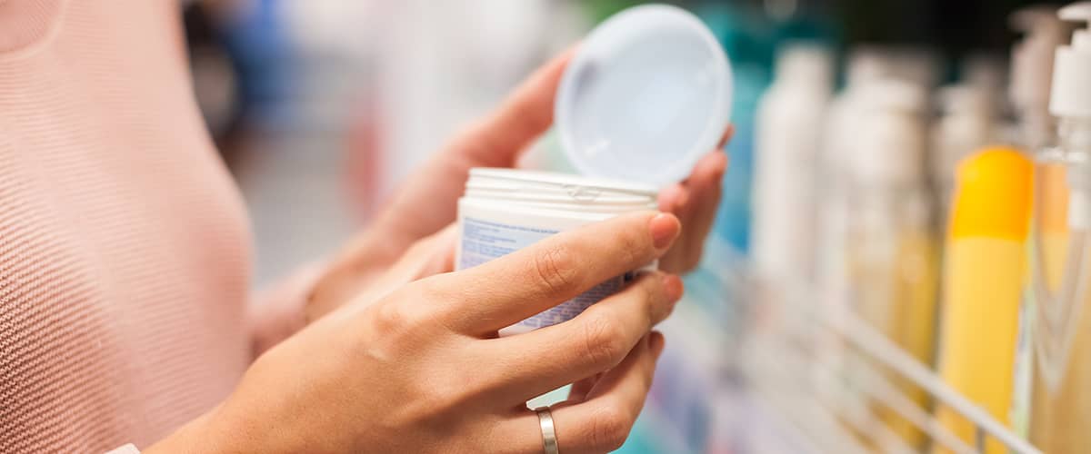 Ženská ruka drží otvorený téglik s krémom