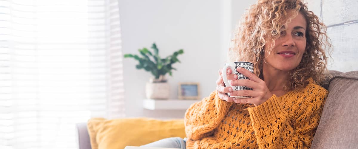 Žena na gauči so šálkou čaju a knihou