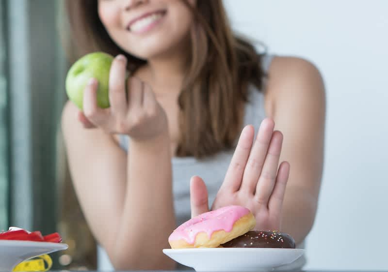 žena s jablkom v ruke odmieta donuty