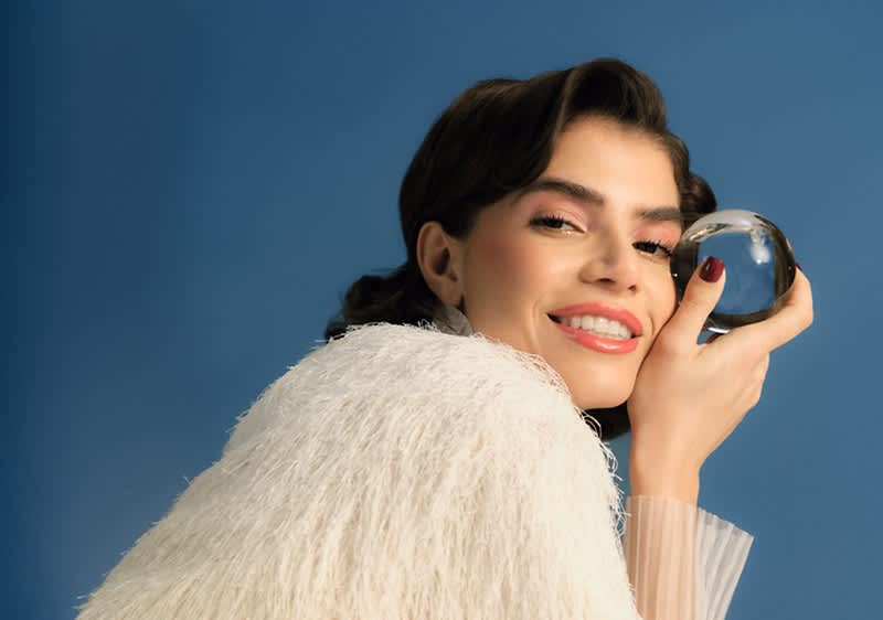 Žena v bielej kožušine drží sklenenú guľu pred modrým pozadím