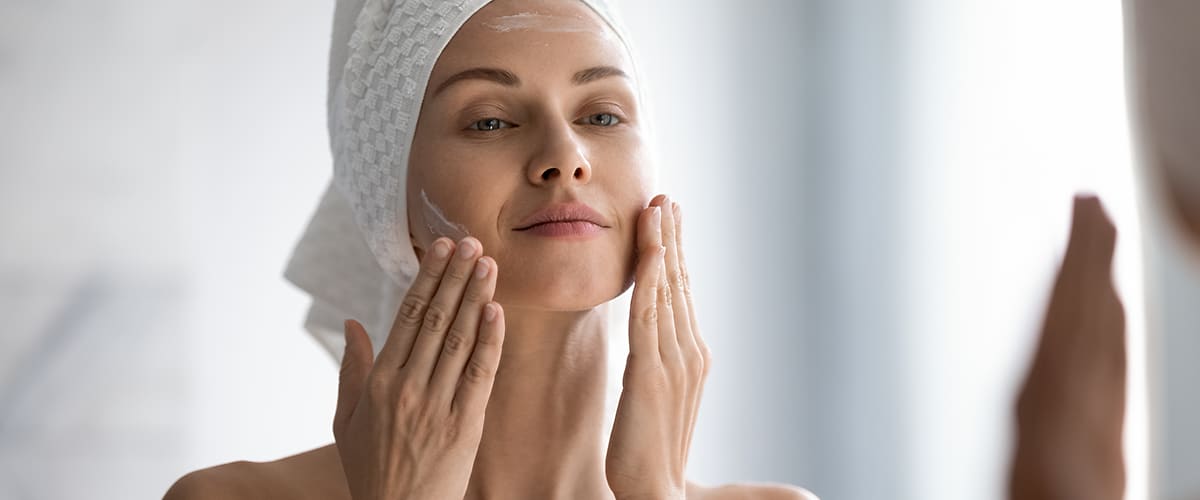 hlava ženy, ktorá si po sprche nanáša na tvár krém