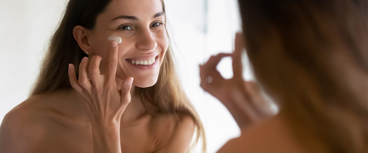 žena pred zrkadlom si nanáša na tvár krém
