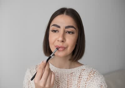 Žena s tmavými vlasmi si nanáša na pery štetcom očné tiene 