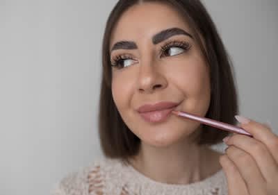 Žena s tmavými vlasmi si kreslí linku okolo pier