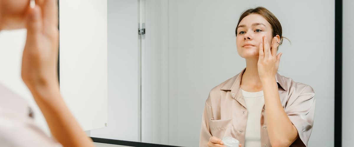 Žena pred zrkadlom si nanáša na tvár krém
