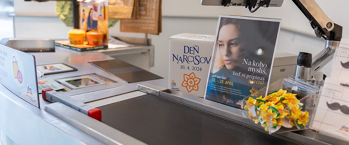 Papierová pokladnička s textom Deň narcisov položená pri pokladnici v dm predajni