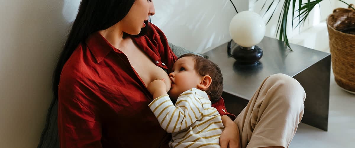 Žena dojčí dieťa na pohovke s lampou v pozadí.