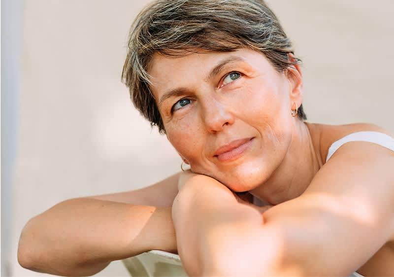 Žena s krátkymi vlasmi a svetlým topom sedí uvoľnene