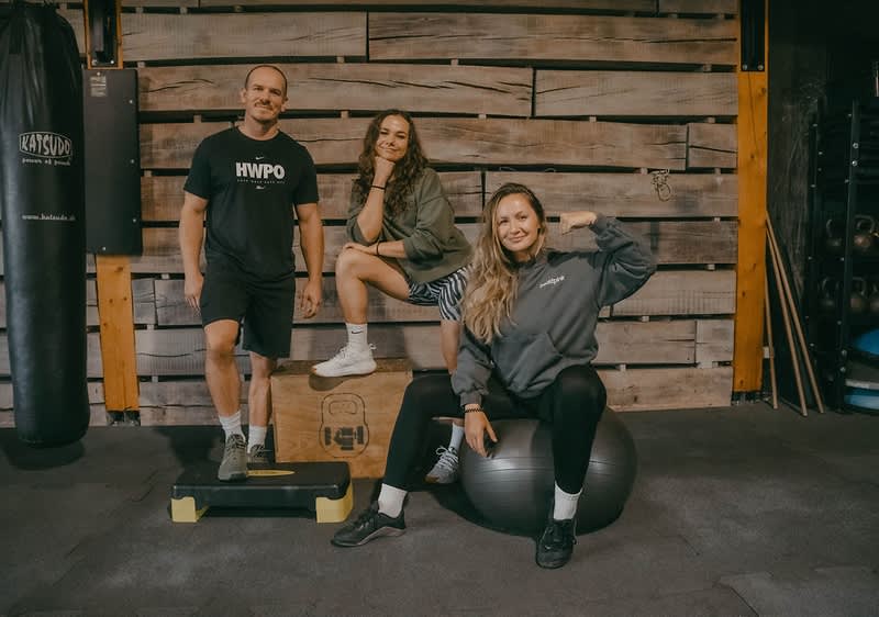 Dve ženy a muž pózujúci na fotografii v posilňovni