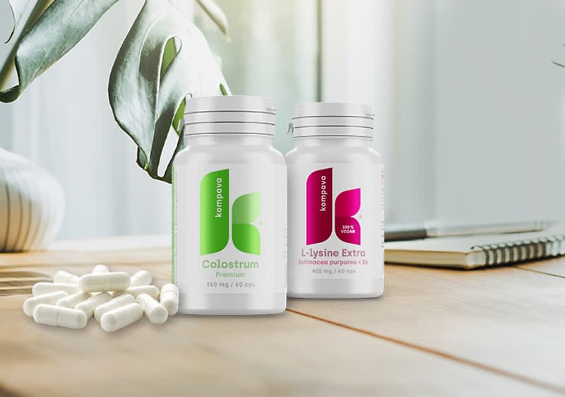 Dva doplnky výživy na stole od zn. Kompava, Colostrum a L-Lysine Extra, vedľa sú biele kapsuly