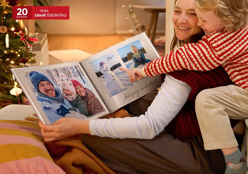 Dieťa s dospelým si prezerajú fotoknihu pri vianočnom stromčeku