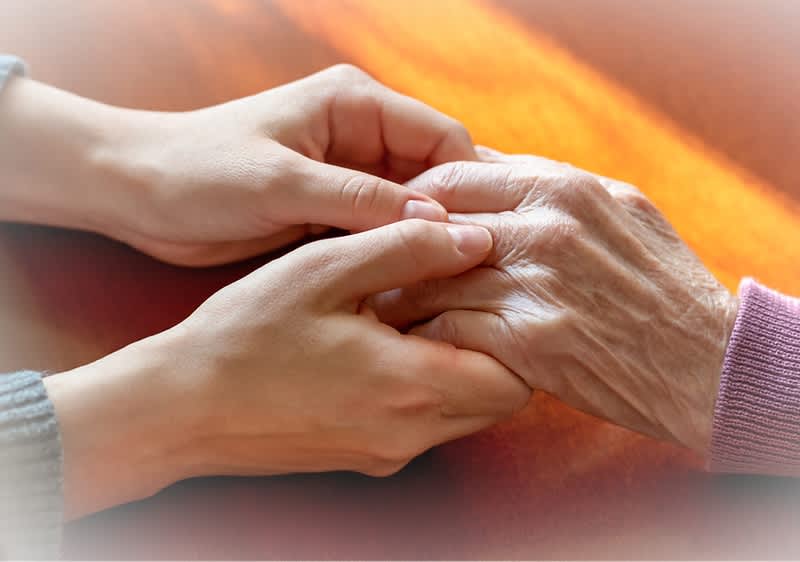 Mladé ruky držia staršie ruky na drevenom stole