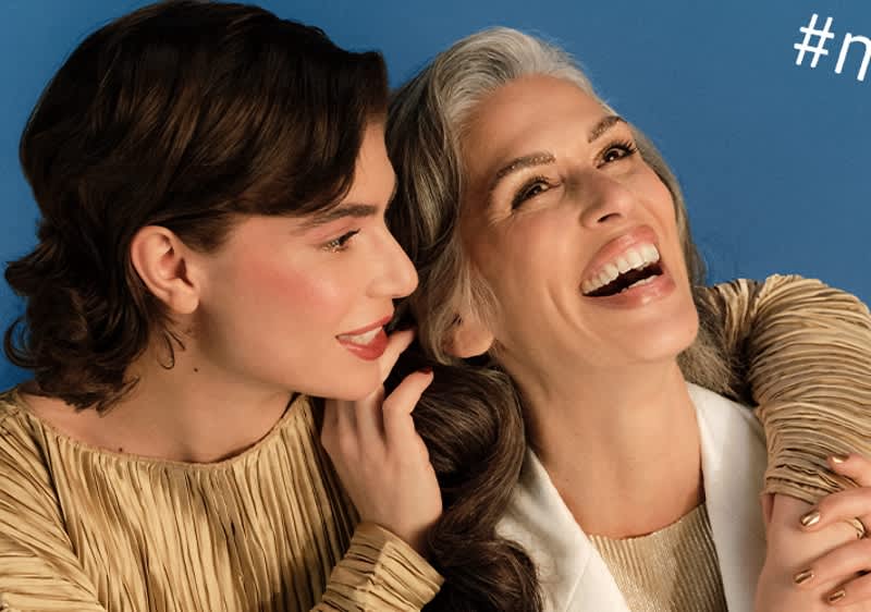 Dve osoby v béžovom oblečení na modrom pozadí s hashtagom v rohu obrázka