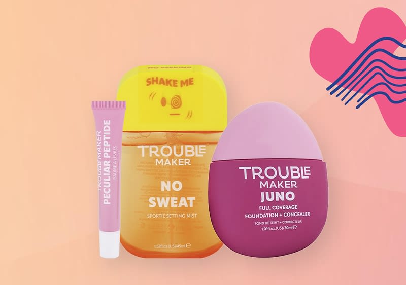 Kozmetické produkty: sprej, korektor a krém značky trouble maker na ružovom pozadí s dekoratívnym prvkom