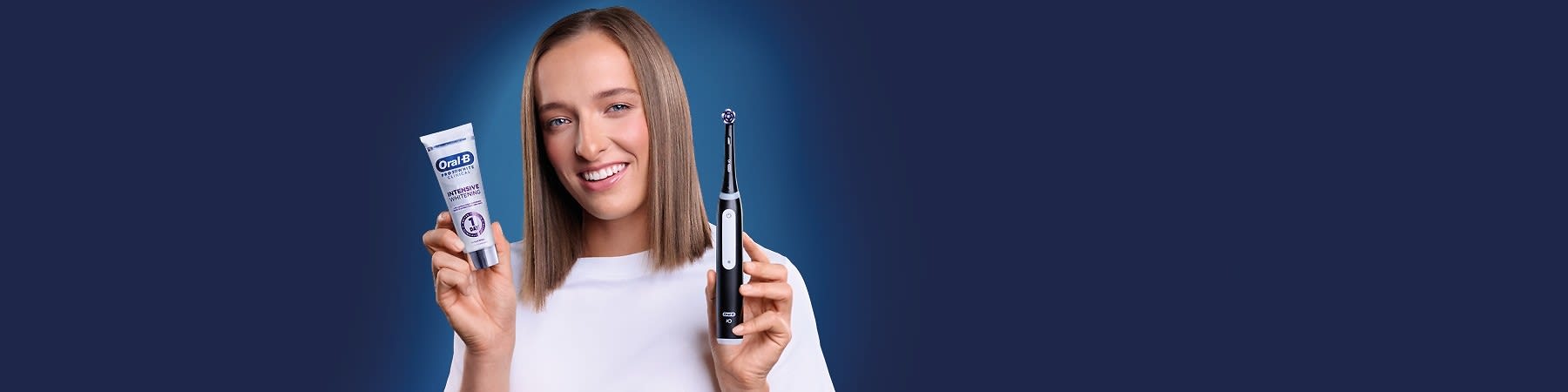 Osoba drží zubnú pastu Oral-B a elektrickú zubnú kefku Oral-B na modrom pozadí.