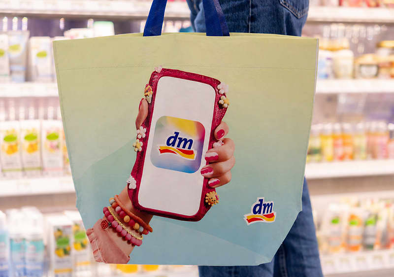 Nákupná taška s logom dm zobrazujúcim telefón a rukou s náramkami