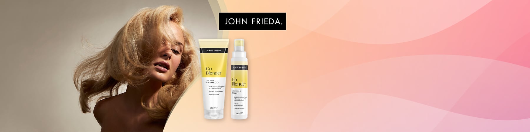 Žena s objemnými nazltozlatými vlasmi vľavo a vpravo dve žlto-biele fľaštičky John Frieda Go Blonder – tubka šampónu 250 ml s nápisom „Go Blonder LIGHTENING SHAMPOO“ a sprej 100 ml s nápisom „Go Blonder LIGHTENING SPRAY“, vpravo hore čierne logo „JOHN FRIEDA“