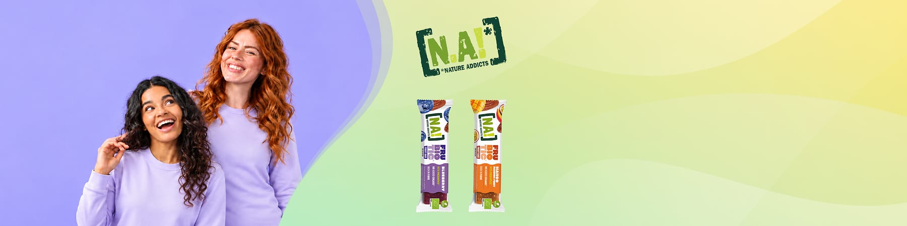 Dve usmievajúce ženy v svetlofialových tričkách vľavo, vpravo logo „N.A! Nature Addicts“ a dva ovocné tyčinky v obaloch.
