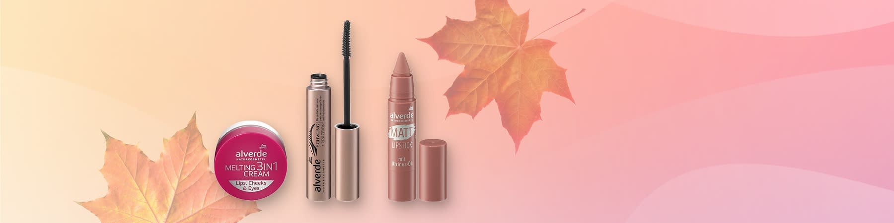 Tri kozmetické produkty značky alverde na svetloružovom pozadí s listom v rohu: zľava malý fľaštičkový krém alverde MELTING 3in1 CREAM s nápisom „Lips, Cheeks & Eyes“, v strede otvorená zlatistá riasenka alverde s viditeľnou čiernou kefkou a nápisom „Schwing“ pri obrázku mihalnice, vpravo matný ceruzkový rúž alverde MATT LIPSTICK s odnímateľným viečkom a textom „mit Rizinus-Öl“