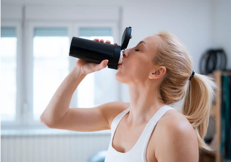 Žena v športovom tielku s copom pije z čiernej shaker fľaše