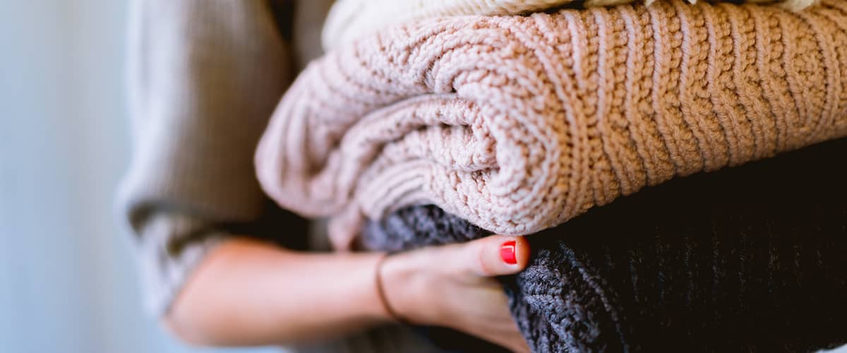 Žena nesie poskladané vlnené svetre.