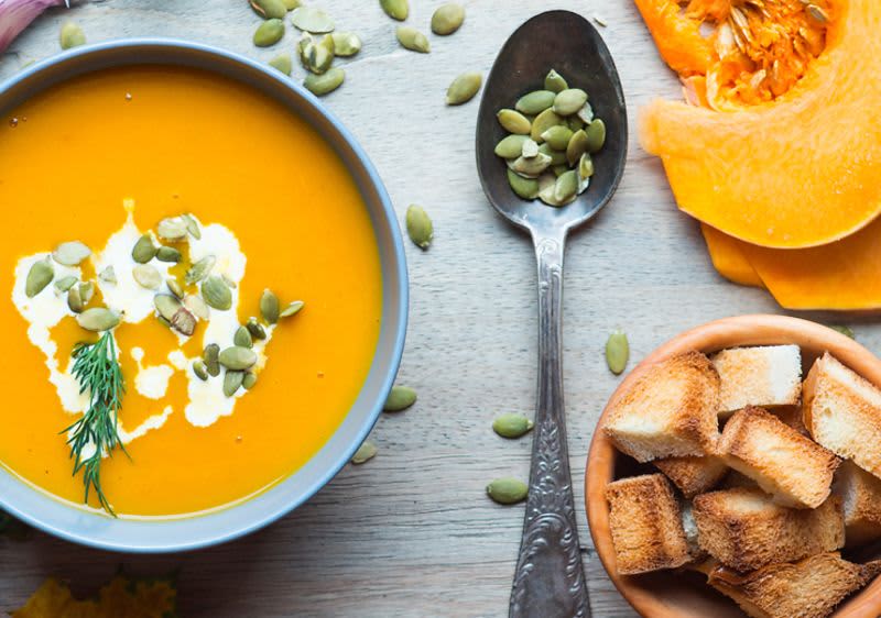 Tekvicová polievka naservírovaná na stole, opečený chlieb, tekvicové jadierka.