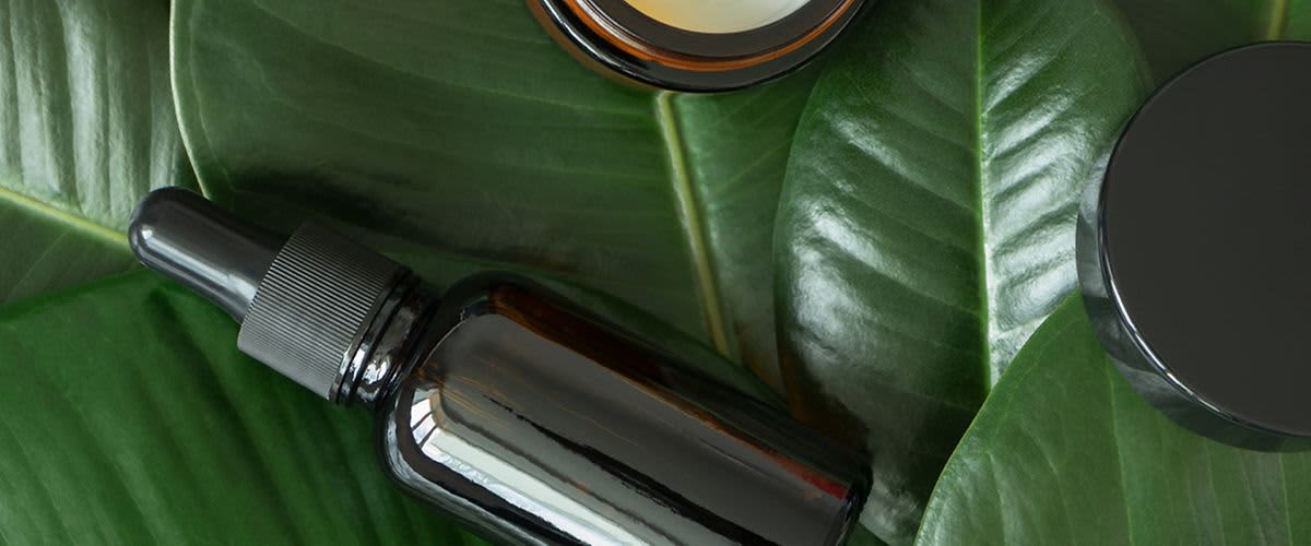 Čajovníkový olej vo fľaške a zelené listy.