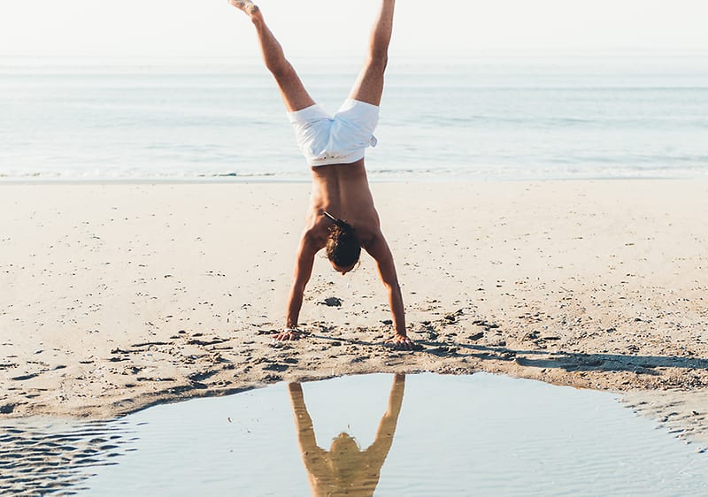 Muž robí stojku na pláži.