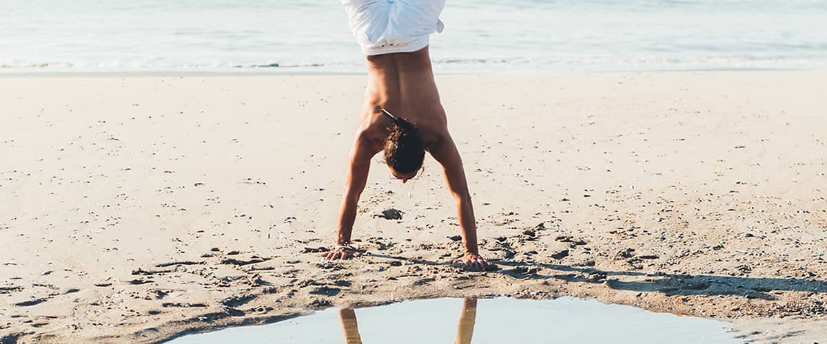 Muž robí stojku na pláži.