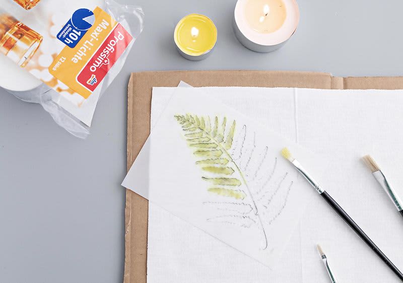 Štetec, čajové sviečky a nanášanie vosku na látku cez šablónu.