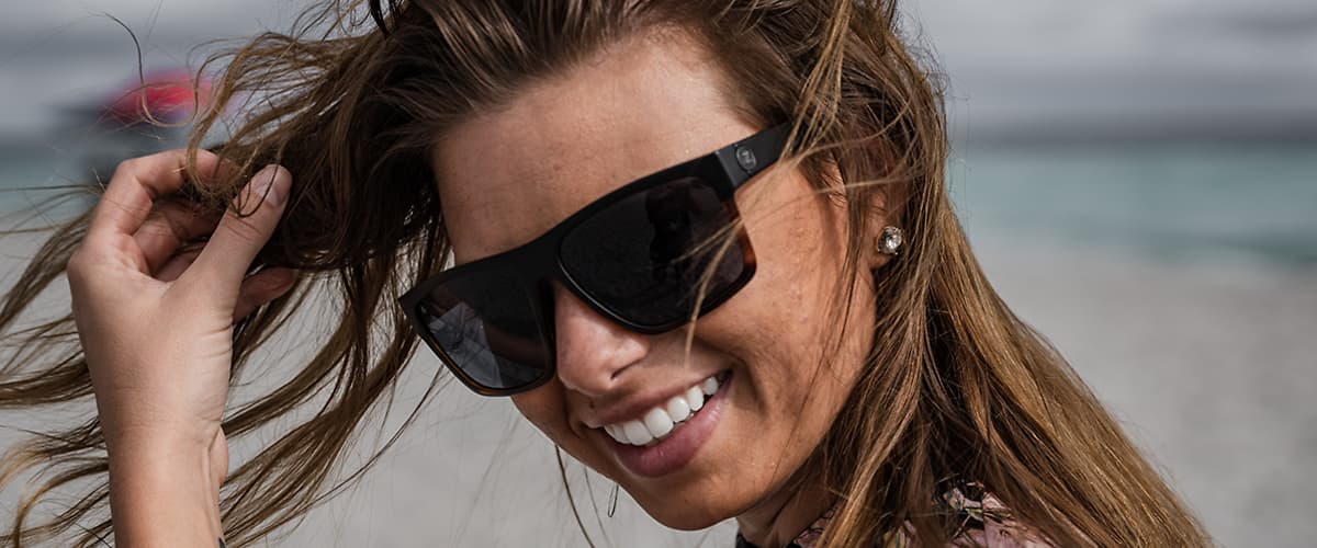 Žena s dlhými vlasmi na pláži v okuliaroch